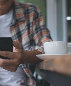 Closeup of man on phone sitting with coffee cup on table